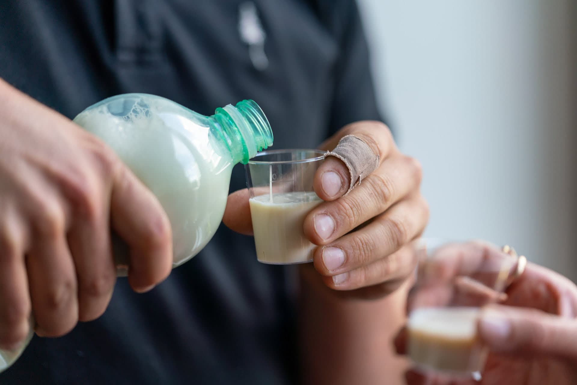 Männerhand giesst im Rahmen einer Degustation von Milchalternativen eine weisse Flüssigkeit in einen Becher